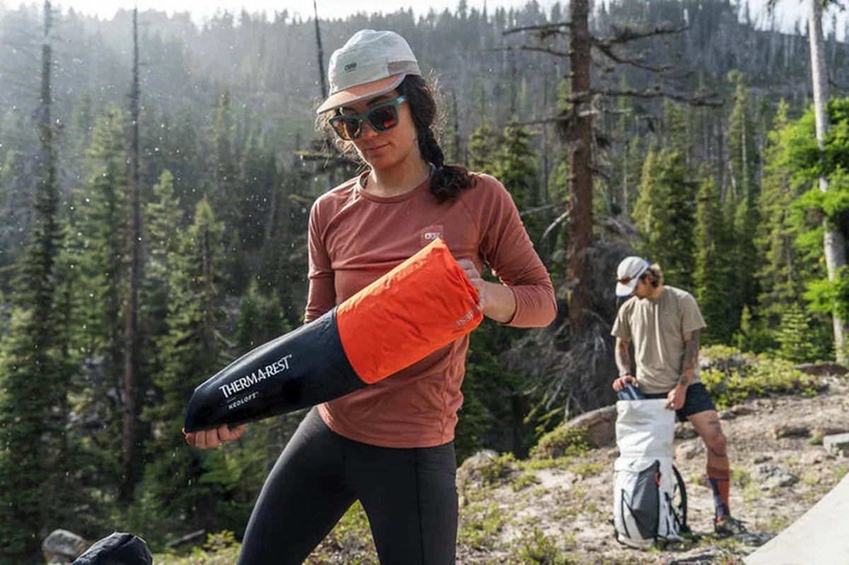 Kvinna packar ner orange NeoLoft liggunderlag i svart påse i skogen