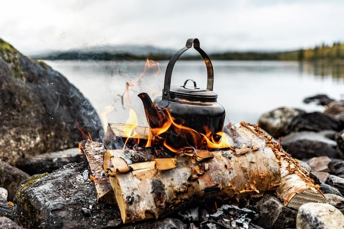 Rostfri kaffepanna sotad över bål vid sjö