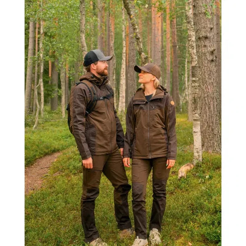 Par som vandrar i skog klädda i mörka Pinewood hybridbyxor och jackor