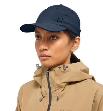 Kvinna bär mörkblå Haglöfs keps med utskuret H-logo och beige jacka