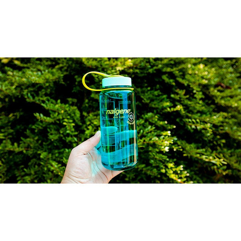 Blå Nalgene vattenflaska med limegrön ögla hållen framför gröna löv, graduerad skala synlig