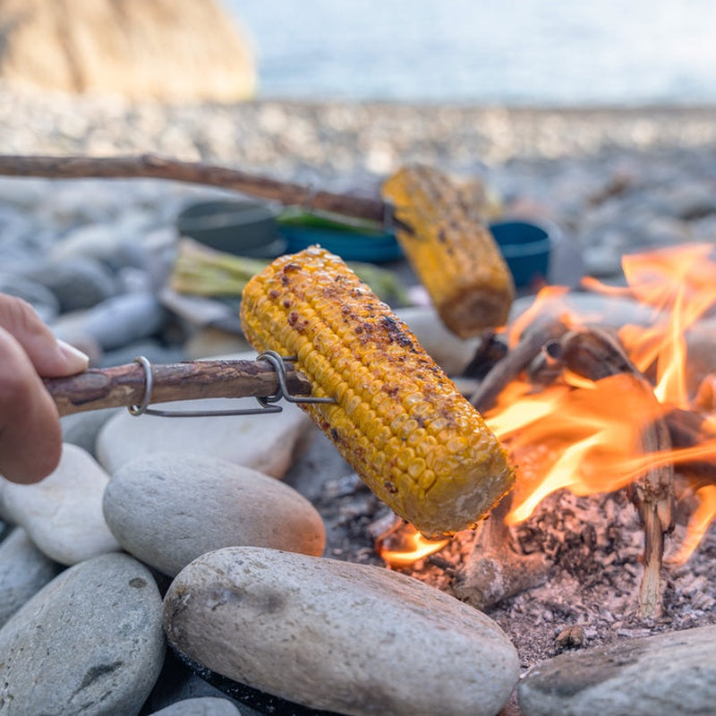 FireFork monterad på pinne med grillad majskolbe över öppen eld