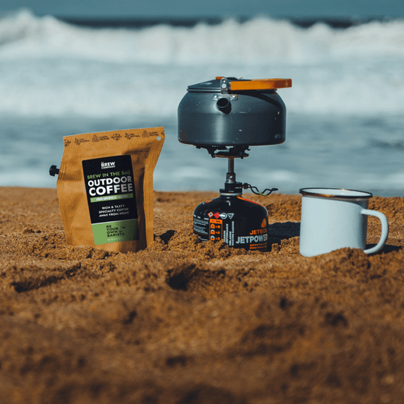 Kaffepåsen vid gasolspisa och enamelkopp på sandstrand