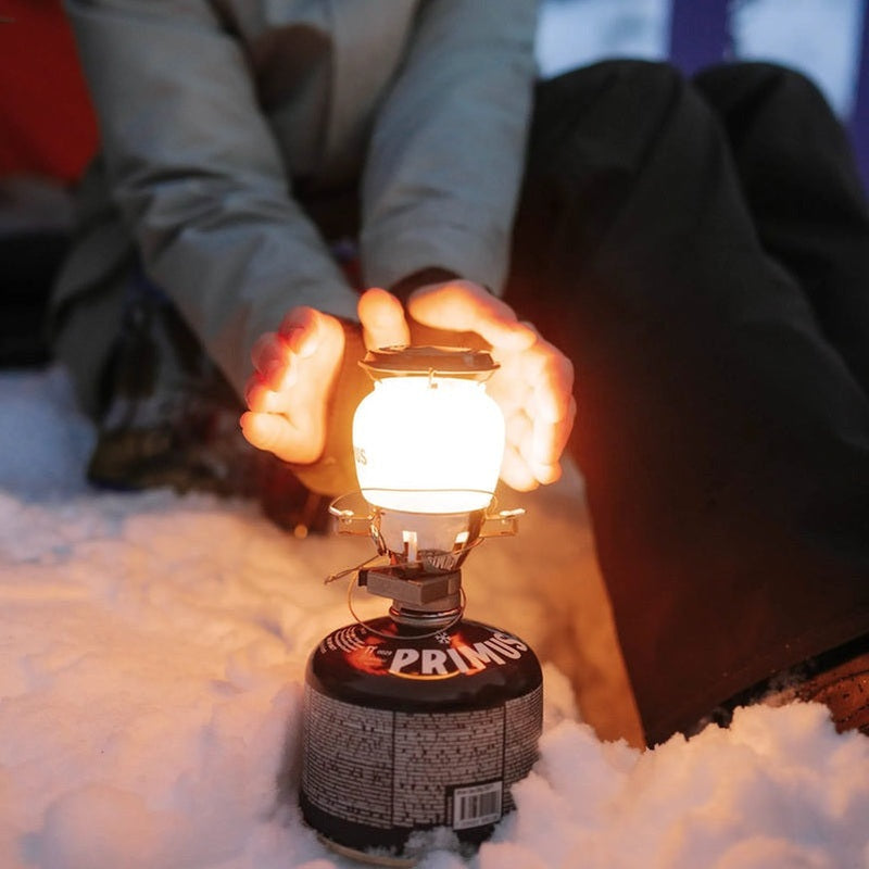 Frostad glaslampa på svart gasbehållare sprider mjukt, varmt ljus i snön