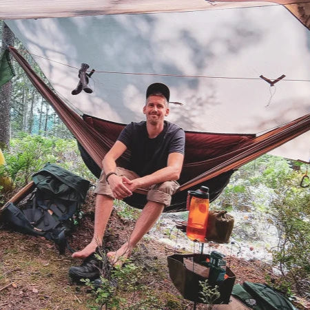 Campingbord i skogen med lykta och vattenflaska