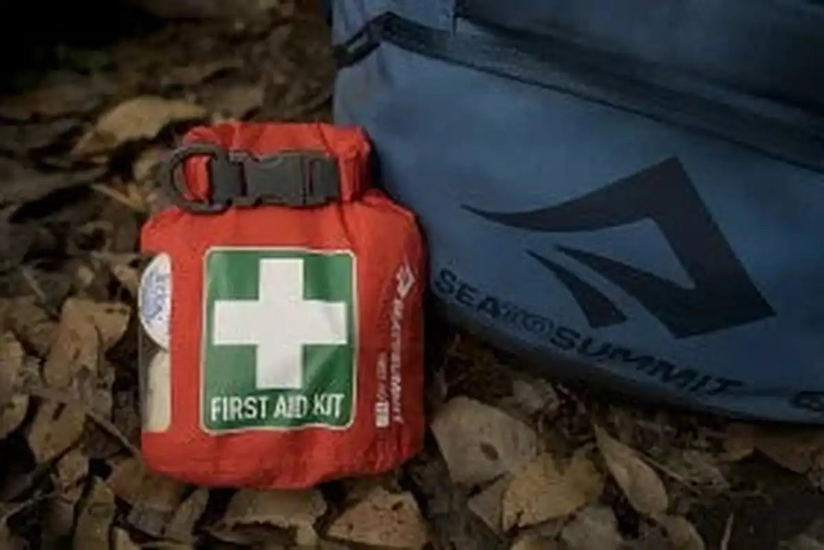 Orange first aid kit placed next to blue backpack outdoors
