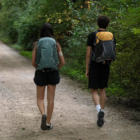 Par som vandrar i skog, kvinna bär teal Osprey ryggsäck